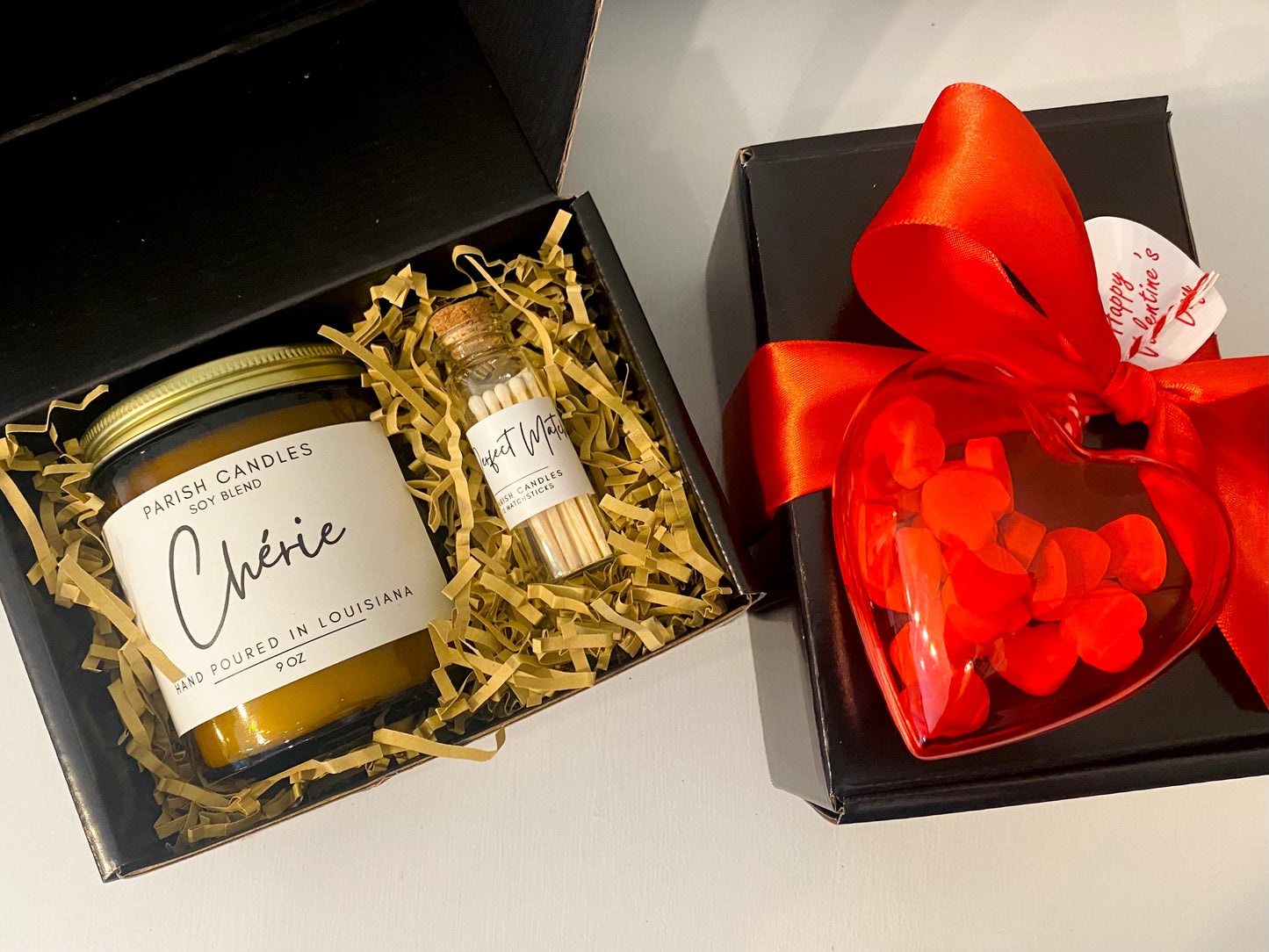 A Valentine's Day themed candle gift set with a 9 oz Parish Candles candle in a glass bottle with a cork stopper, a red ribbon, and a decorative ornament.