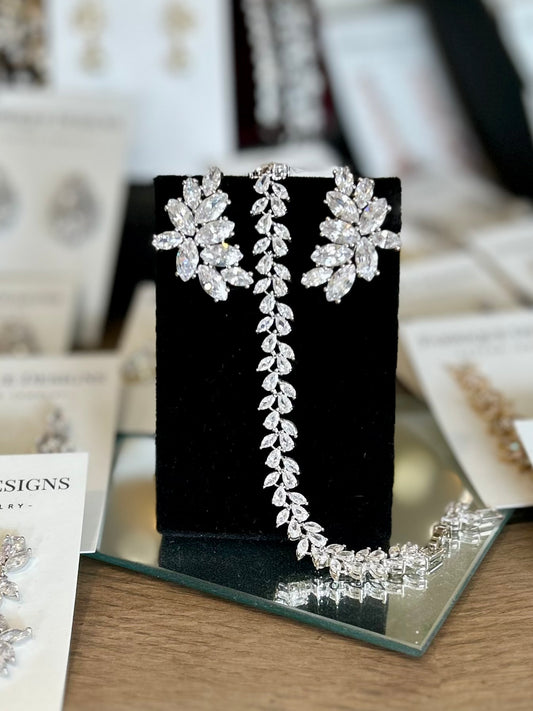 A pair of silver-colored rhinestone cluster earrings displayed on a black stand, with a post back closure.