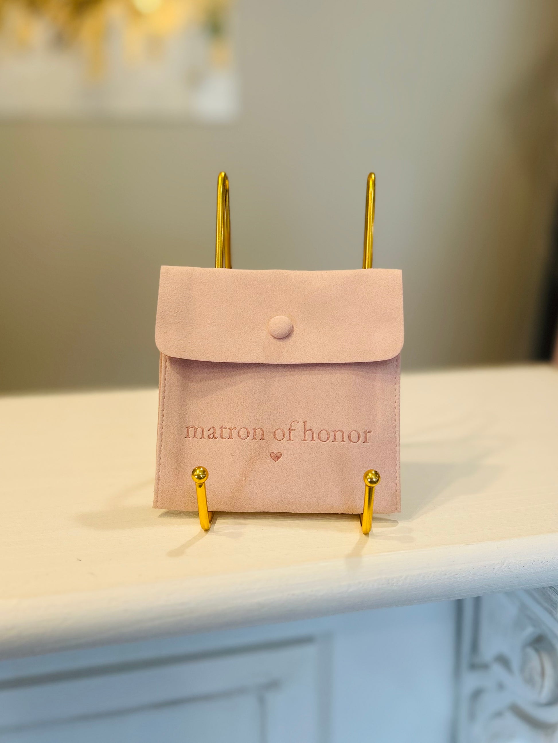 Pink pouch with 'matron of honor' text on a white surface