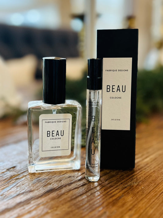 A bottle of BEAU by Fabrique Designs cologne, accompanied by its black packaging box. The bottle is clear with a black cap, and the box is also black with the brand and product name visible.