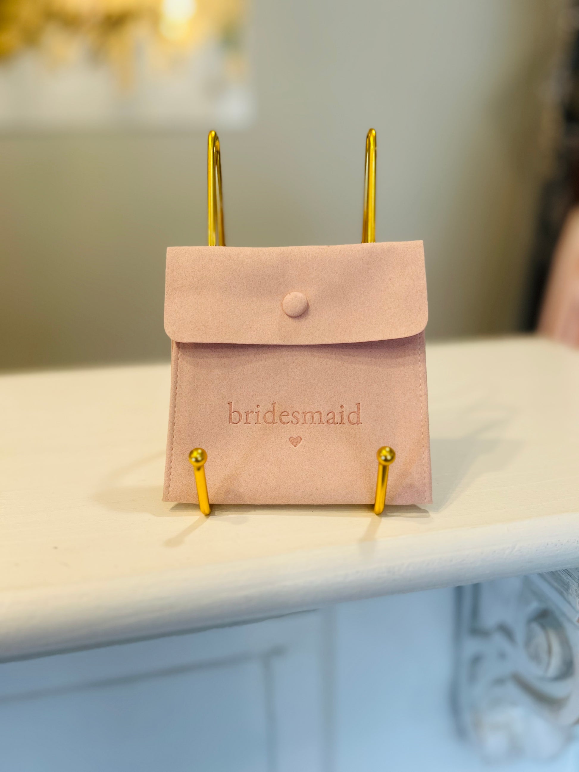 Pink pouch with 'bridesmaid' text on a stand against a blurred background