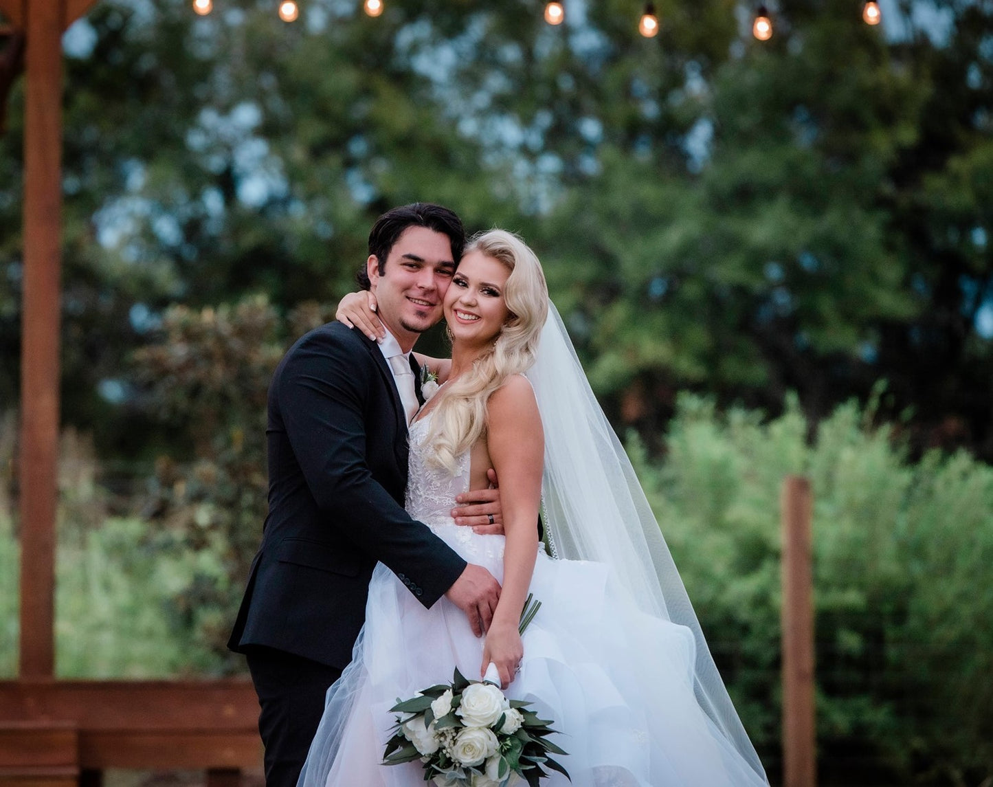 A bride and groom standing outside in front of a pergola.