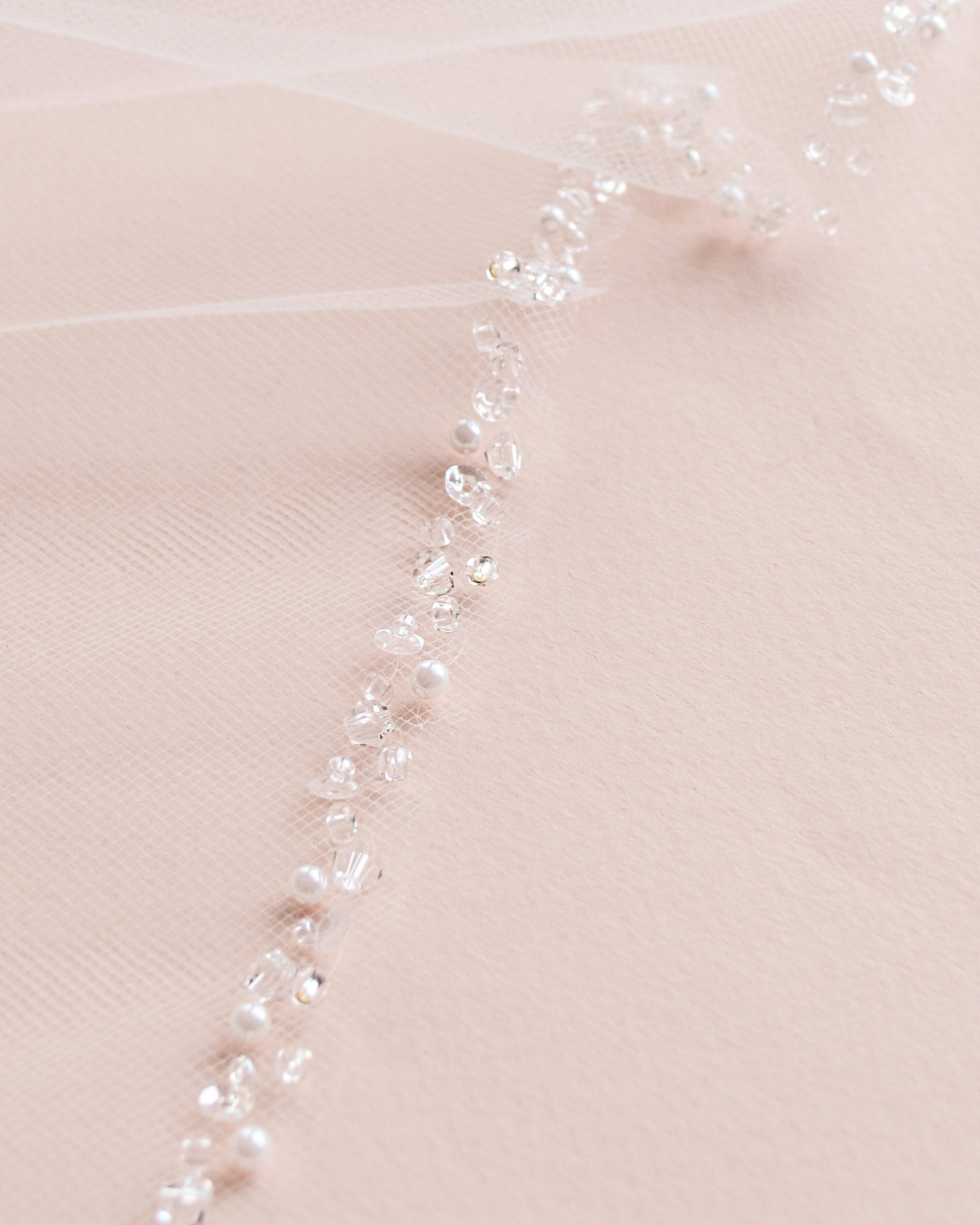 Close up of off white veil with pearls and embellishments on the edge.