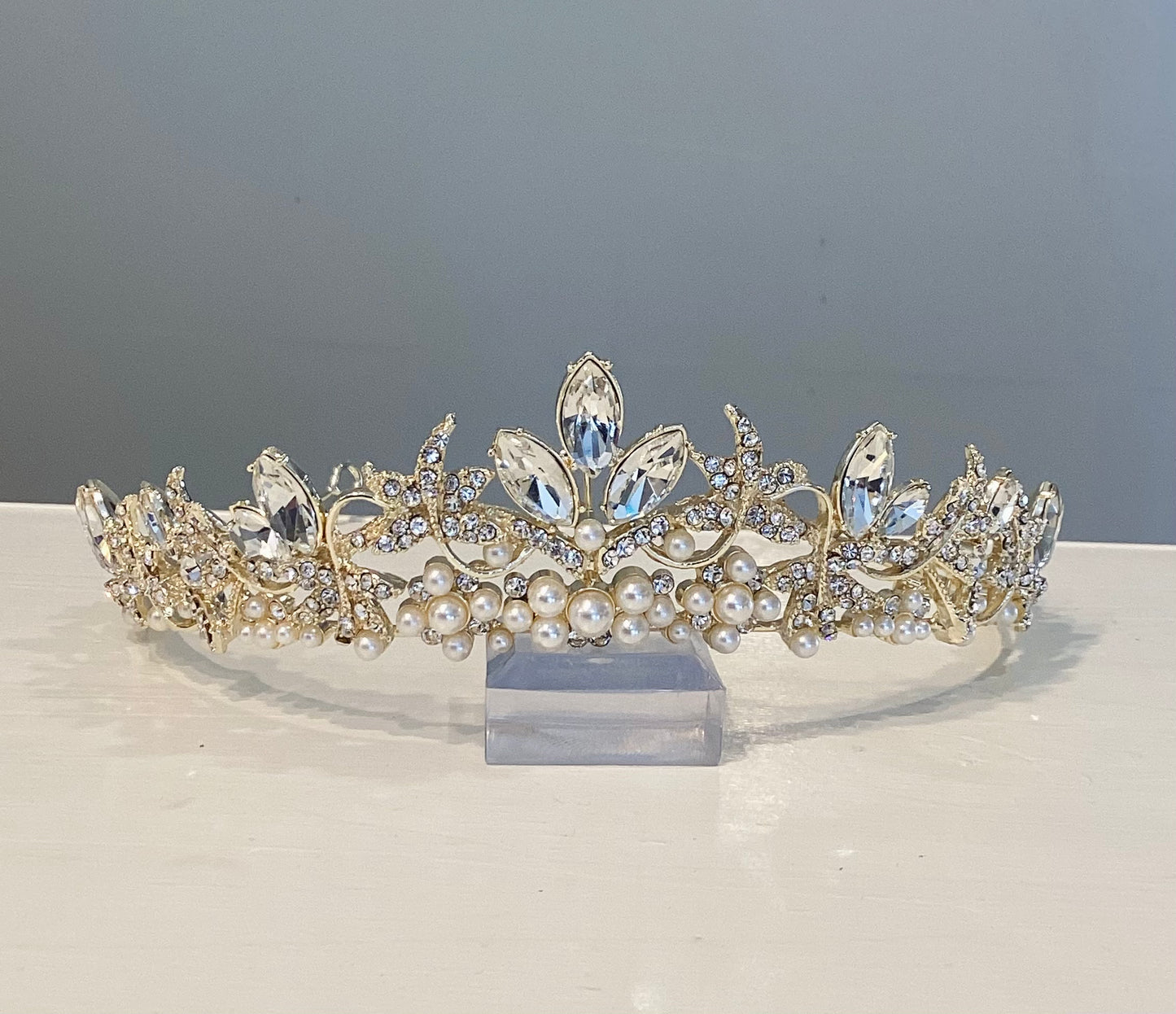 Gold tiara with pearls and rhinestones on a white counter.
