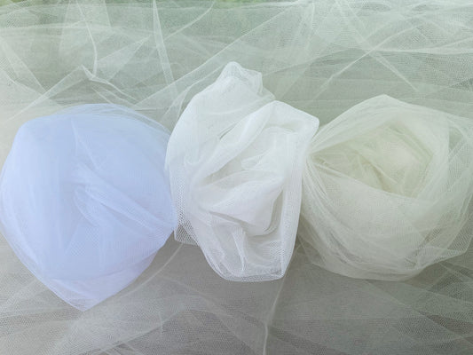 Three bridal veils in white, off white, and cream colors, displayed in a transparent state, with a blurred background.