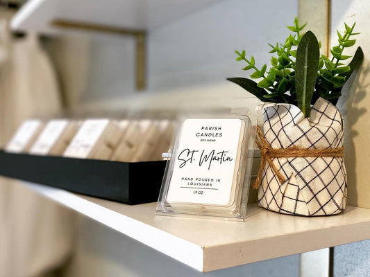 A warmer melt candle with a label that reads 'St. Martin', placed on a shelf with a black lid on top and a small candle warmer with a white and black checkered design.